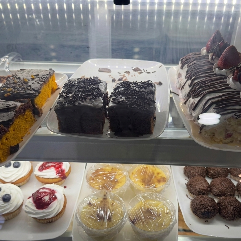 Glass dessert display case filled with chocolate cakes, cream-and-strawberry roll, cupcakes, puddings, and chocolate truffles.